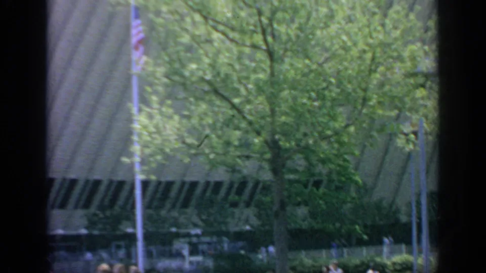 1964 Flushing Meadows frame with trees, an American flag, landscaped grounds, and a modernist building viewed through window-like borders.