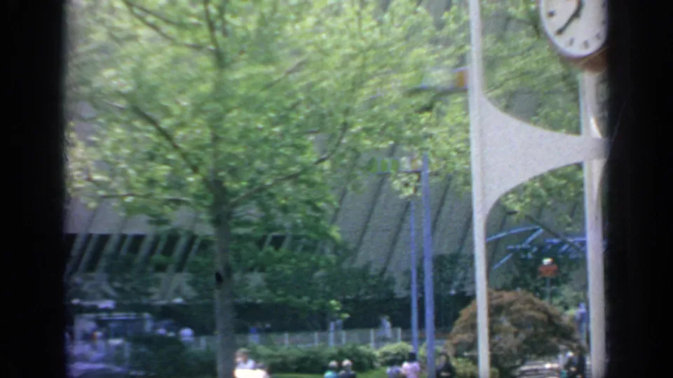 1964 Flushing Meadows frame showing a modernist clock structure, trees, landscaping, and partial fairground architecture.