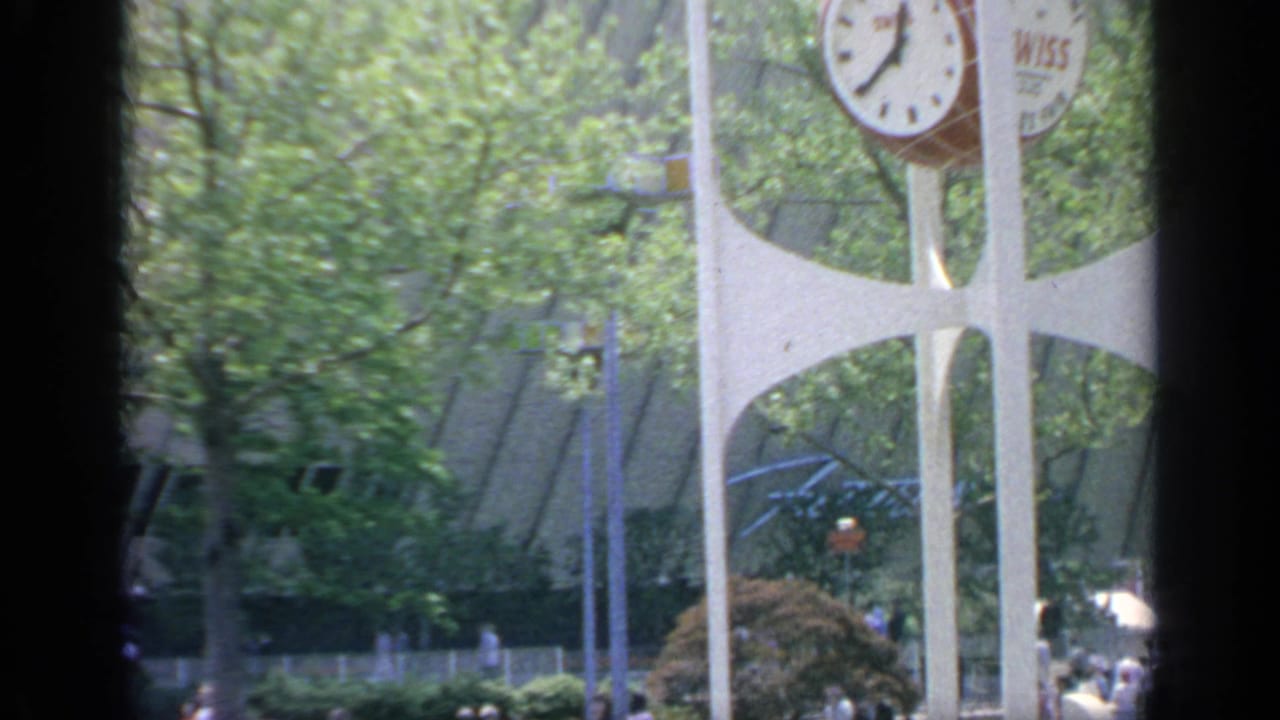 Wiss clock tower seen through dark film borders with trees and distant fair visitors.