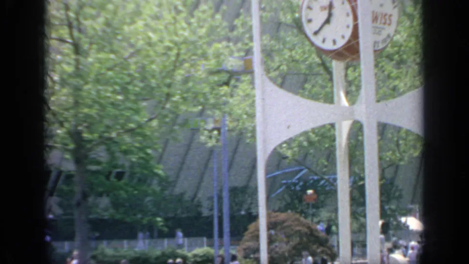 1964 Flushing Meadows World's Fair view of the white Wiss clock tower among trees, with distant visitors below.