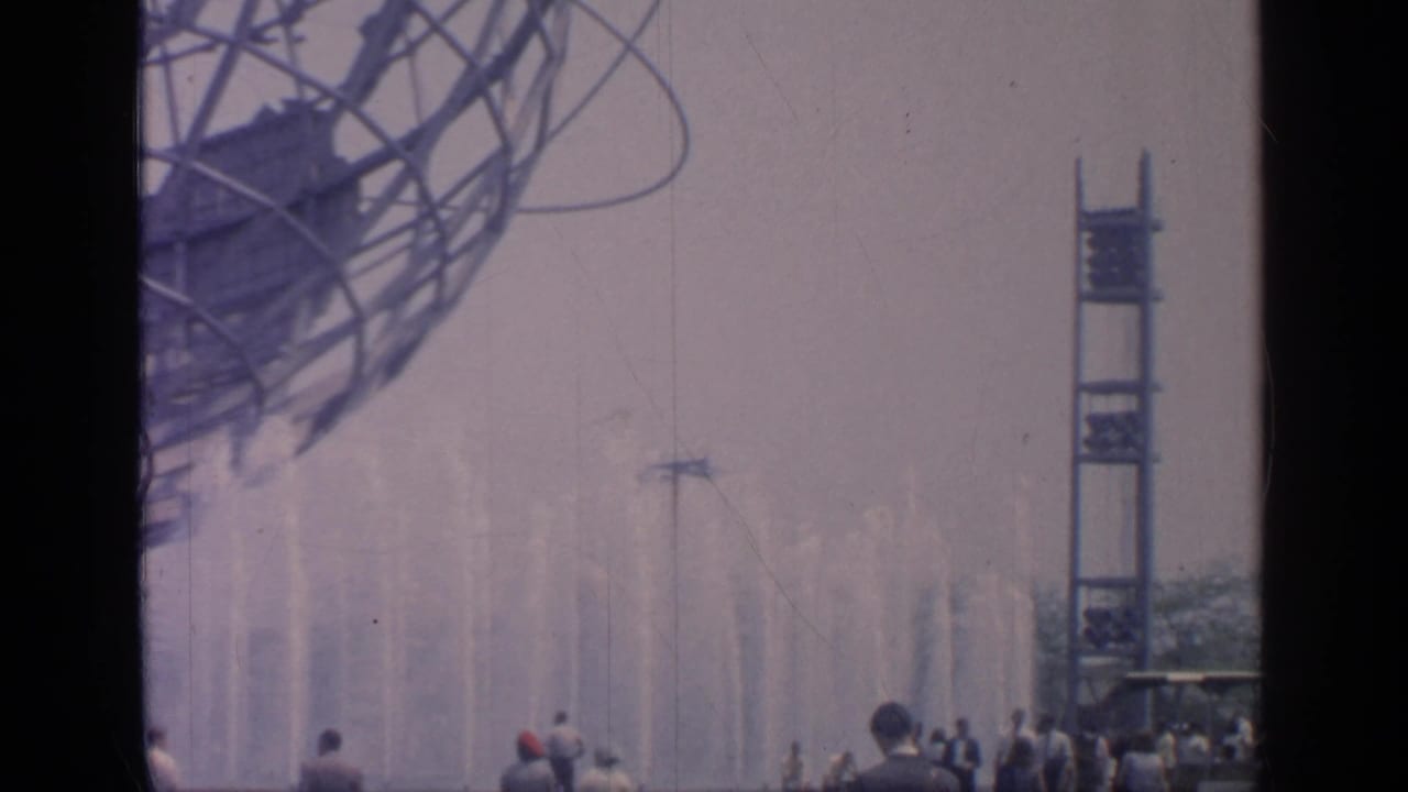 Fountains spray below the Unisphere with a tower and visitors in the distance.