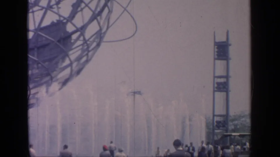 The Unisphere and fountain field at Flushing Meadows, with distant fair visitors and a vertical tower at right.