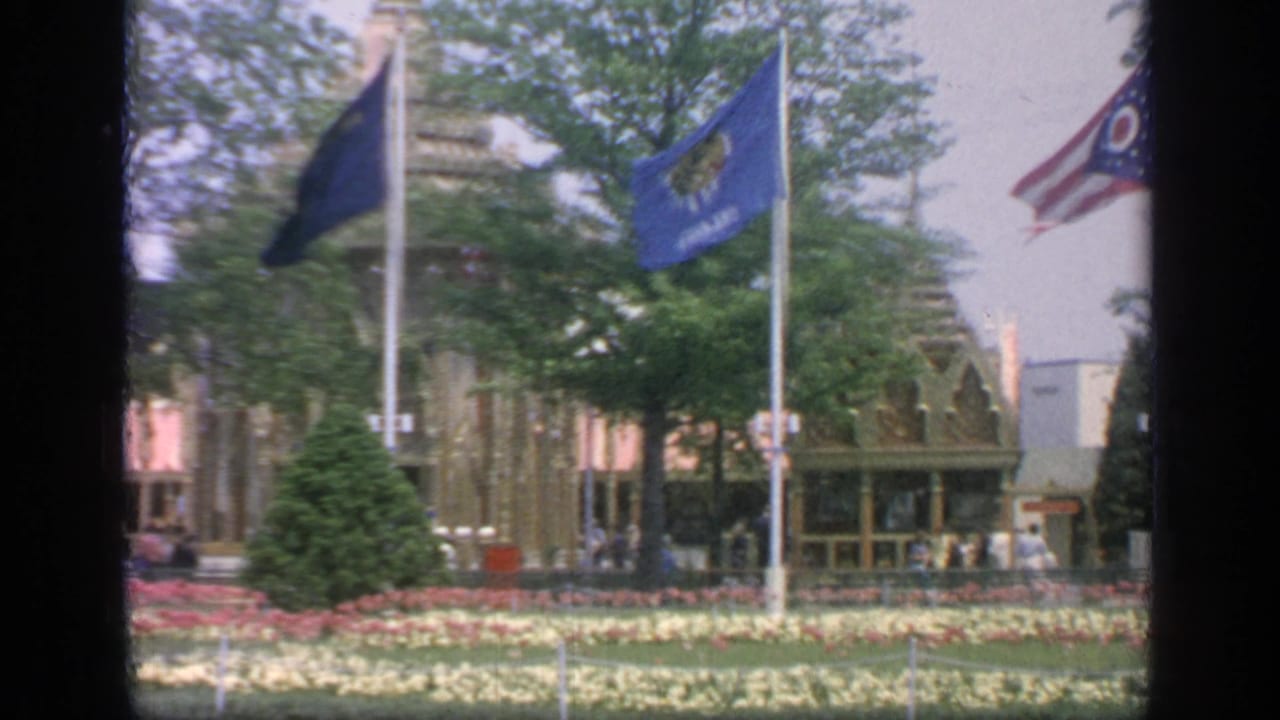 Flags above flower beds and trimmed shrubs with fair buildings and trees in the background.