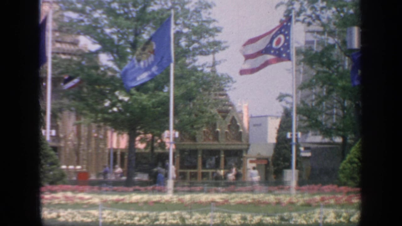 Ohio flag, blue banner, flower beds, trees, and pavilion details seen through a dark frame.