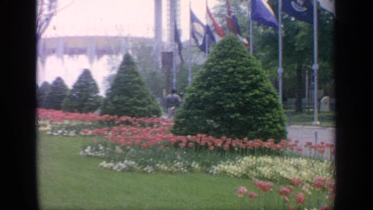Fountain spray, flags, flower beds, lawn, and trimmed evergreens.