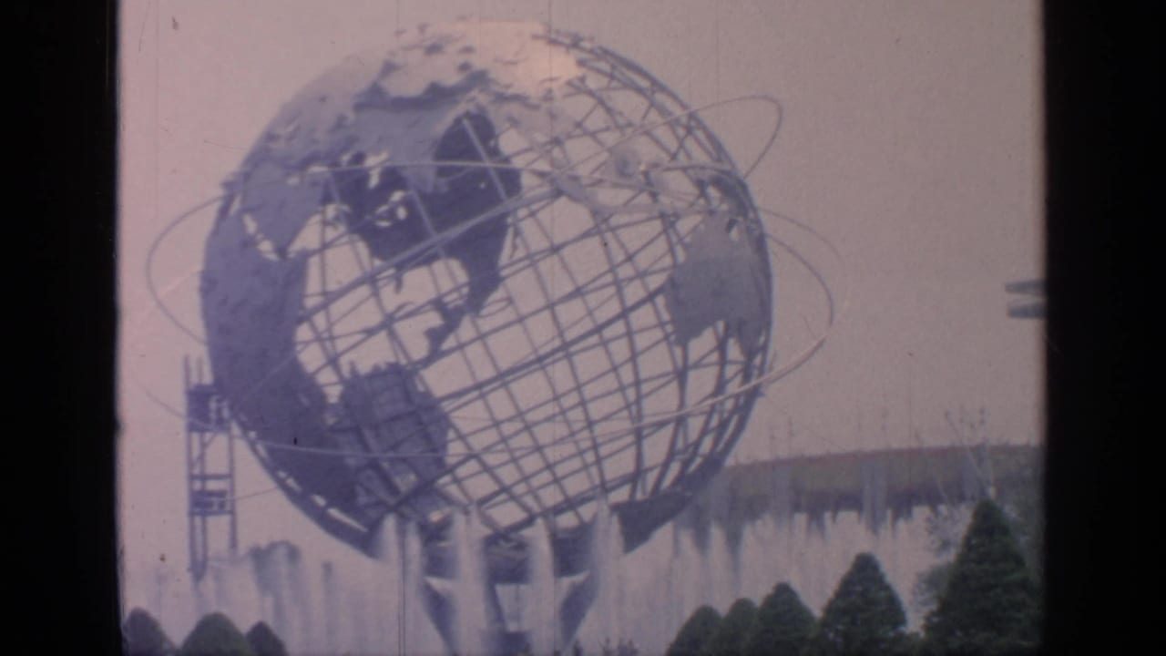 Metal globe sculpture and fountains with shrubs and a tower-like structure nearby.