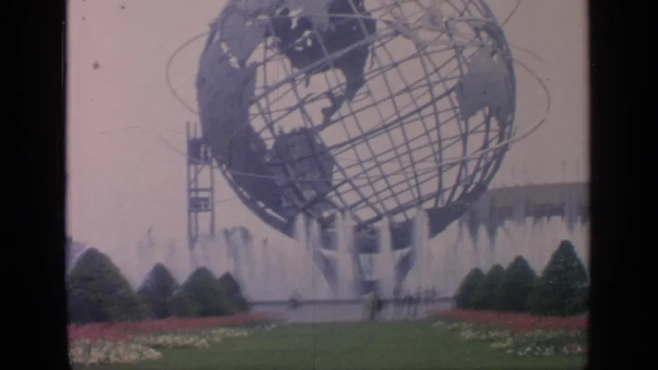 Home-movie frame of the Unisphere at the 1964 New York World's Fair, seen above fountains and planted beds.