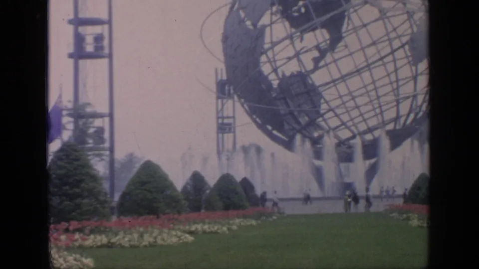 Wide visitor-shot view at Flushing Meadows showing the Unisphere, fountains, planted beds, and people on the grounds.