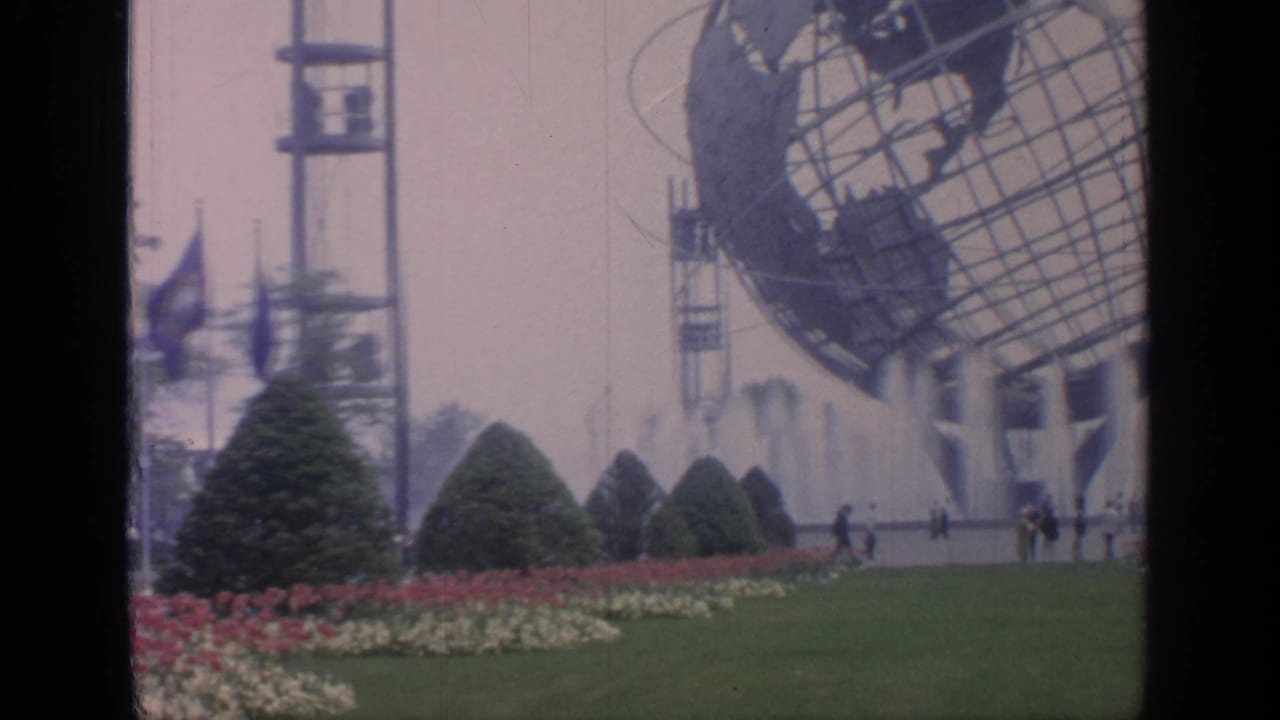 Unisphere, fountains, flowerbeds, trimmed shrubs, and distant visitors at fairgrounds.