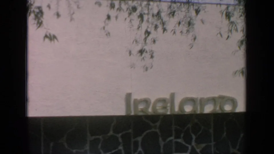 Visitor-shot 8mm view of the Ireland pavilion lettering at Flushing Meadows, partly obscured by framing and foliage.