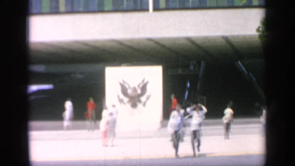 1964 Flushing Meadows plaza with visitors near a large white sign or panel featuring an eagle emblem.