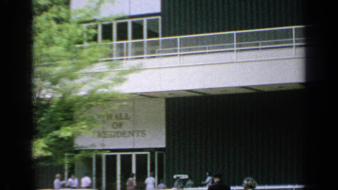 Hall of Residents entrance with trees, balcony railings, and people near the doors.