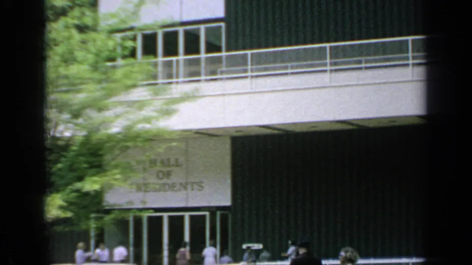 Hall of Residents exterior at the 1964 World's Fair, with visitors near glass doors below a balcony and tree cover.