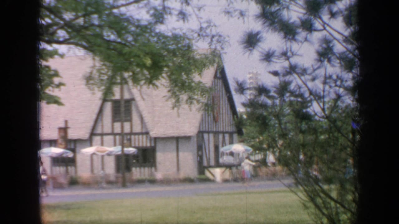 Tudor-style building seen through trees with umbrellas and lawn in front.