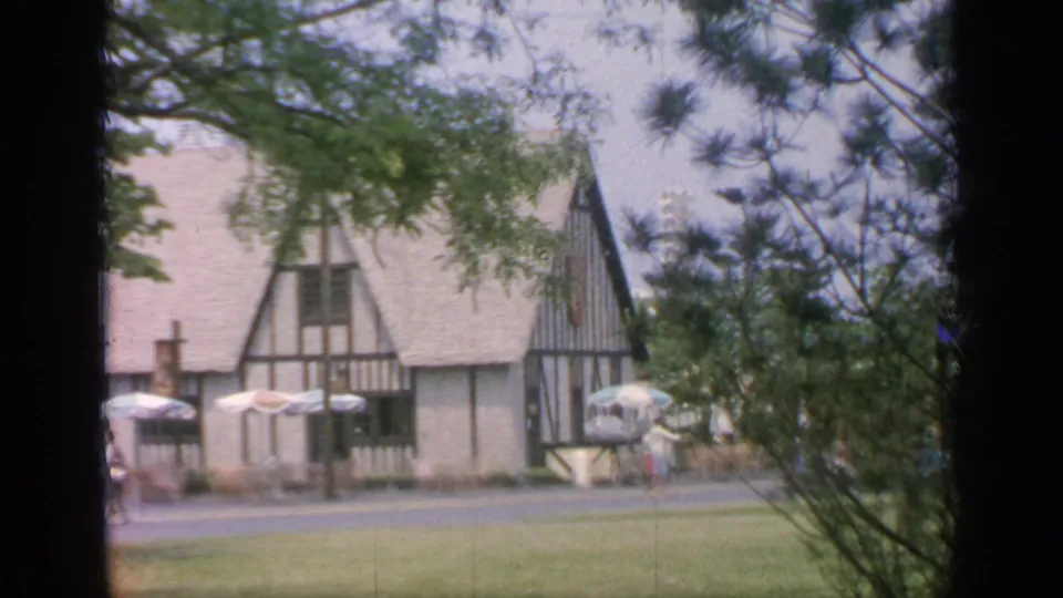 1964 Flushing Meadows view of a Tudor-style fairground building across a lawn, partly framed by trees.