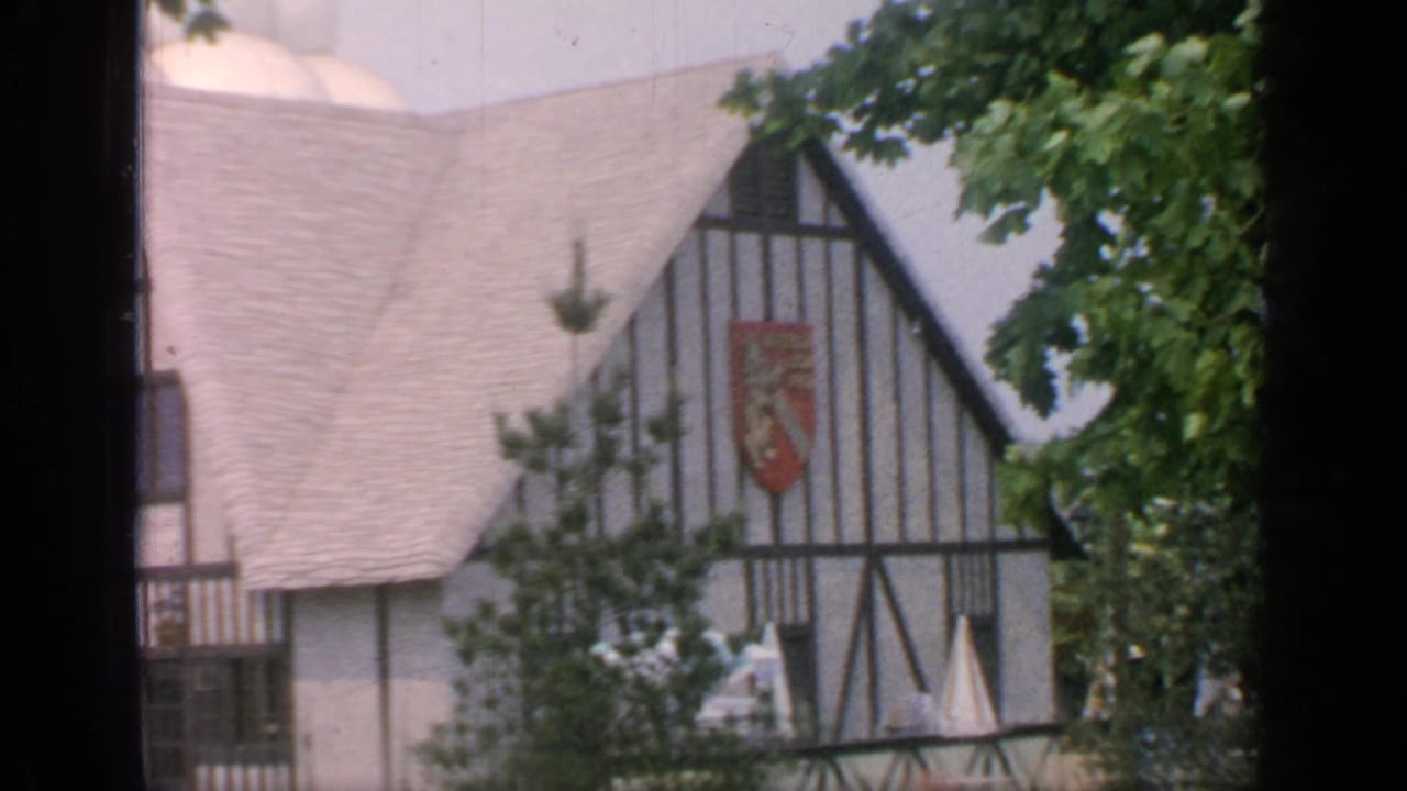 Closer view of a Tudor-style building with a red shield emblem and pale roof.