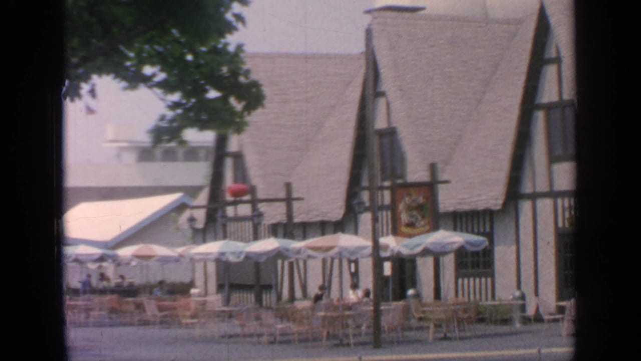 Outdoor food court with empty tables, umbrellas, and a Tudor-style building.