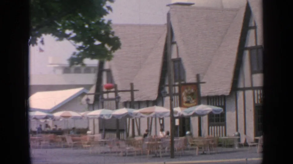 1964 Flushing Meadows fairground view of empty outdoor seating beside a Tudor-style food building and patio umbrellas.