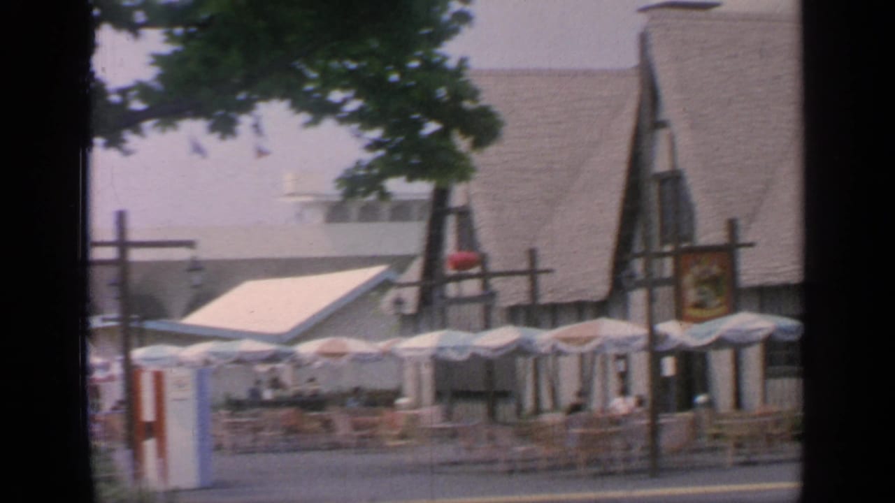 1964 Flushing Meadows outdoor dining area with empty chairs, umbrellas, a gabled facade, and a small red-and-white booth.