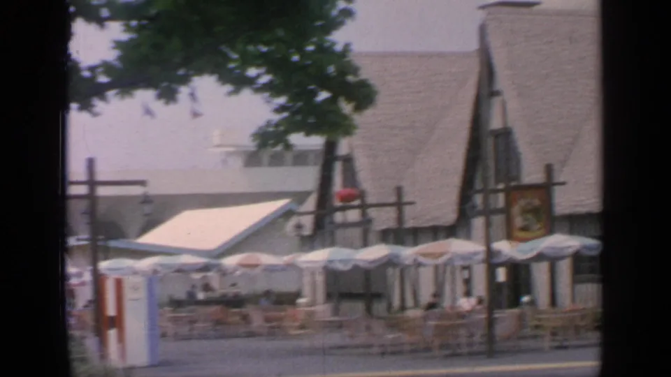 1964 Flushing Meadows outdoor dining area with empty chairs, umbrellas, a gabled facade, and a small red-and-white booth.