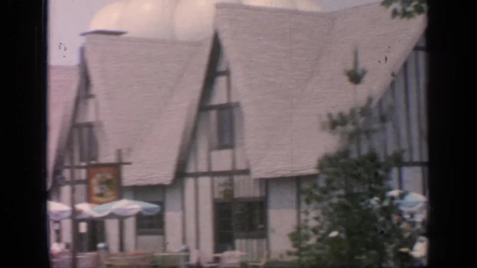 Closer 1964 fairground view of the Tudor-style building roofline, hanging sign, and mostly empty outdoor dining area.