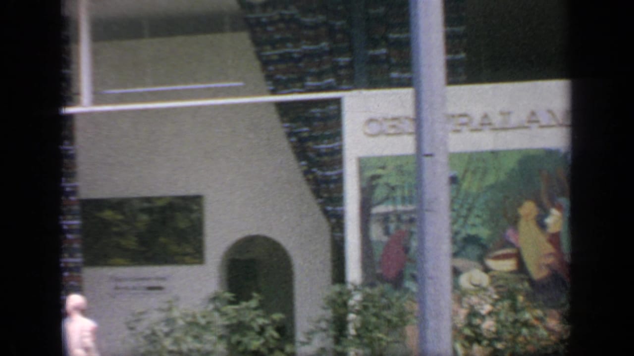 Pavilion exterior with Central America mural, arched doorway, greenery, and a visitor nearby.