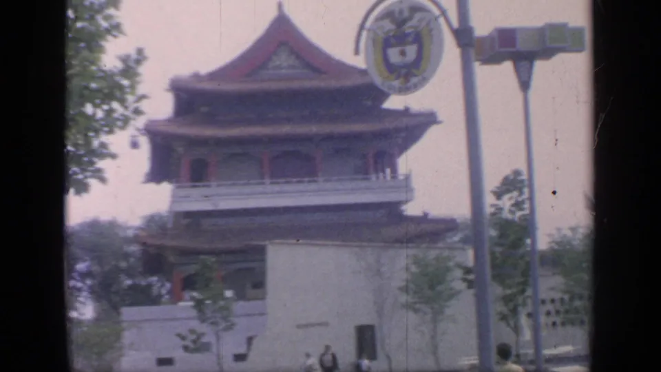 1964 Flushing Meadows fairground frame with a Chinese-style pagoda, round sign, lamp posts, young trees, and visitors near the lower edge.