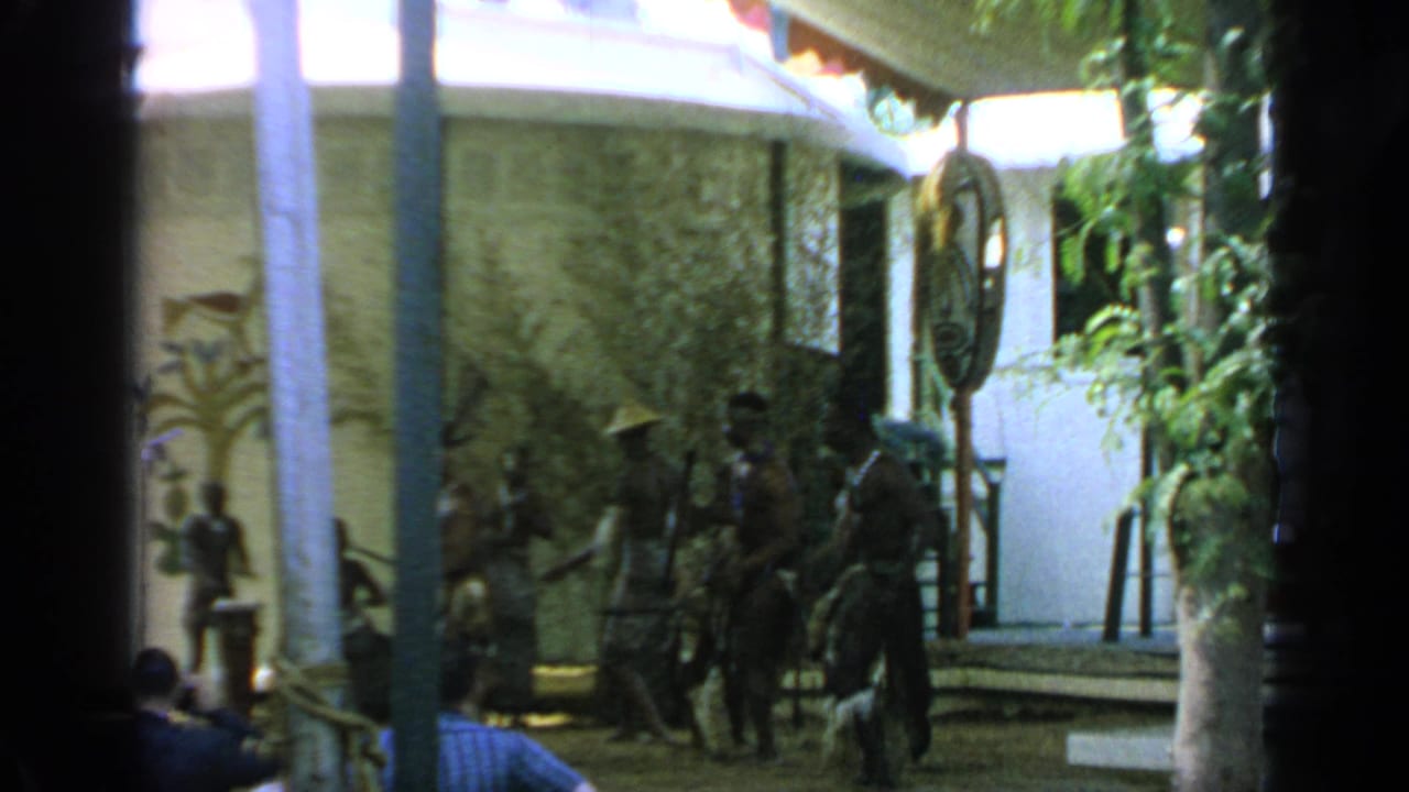 Distant performers under a white tent with trees and stage decorations around them.