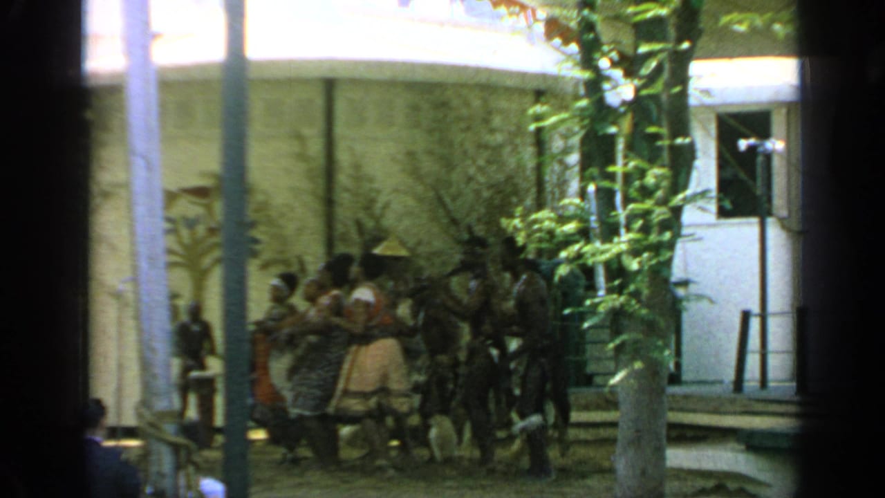 Dancers perform near a crowd in a courtyard with columns and trees.