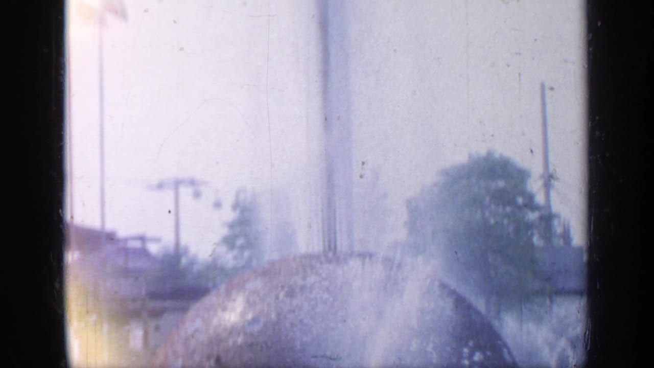 Fountain spray rises around a large spherical structure with trees and poles in the background.