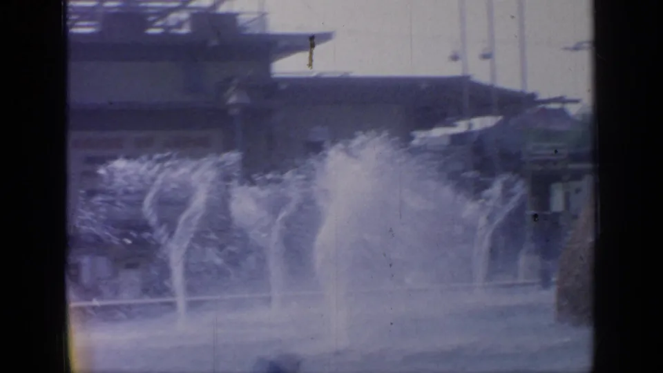 1964 Flushing Meadows fountain scene with multiple water jets, low structures, and soft handheld 8mm framing.