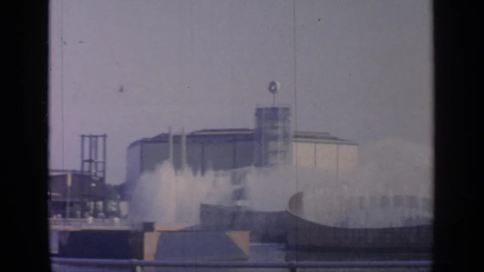 A 1964 Flushing Meadows view shows fountain spray, a broad modernist building, railings, and a hazy sky in soft 8mm color.