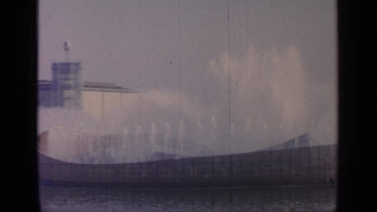 At Flushing Meadows in 1964, misting fountains fill the view while the distant Unisphere form and fairground architecture appear through haze.