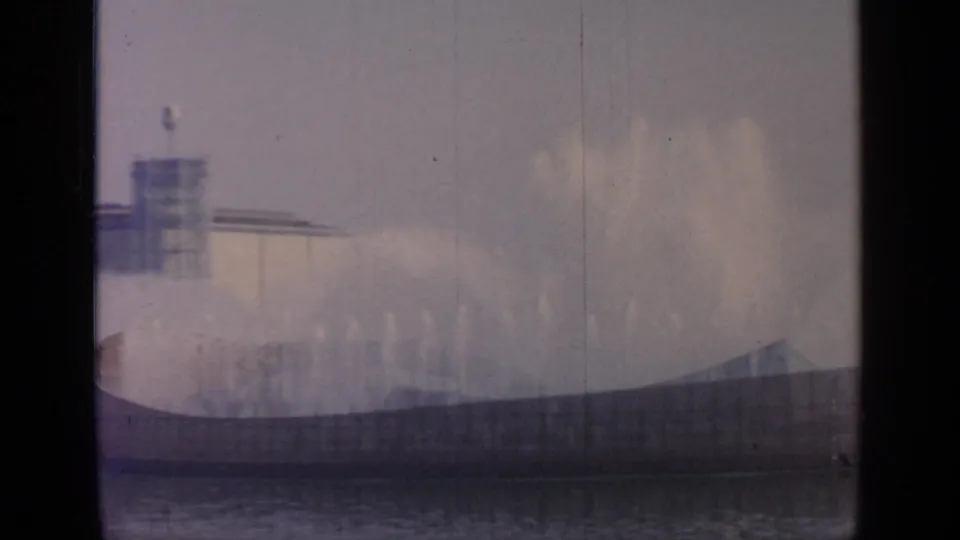 At Flushing Meadows in 1964, misting fountains fill the view while the distant Unisphere form and fairground architecture appear through haze.
