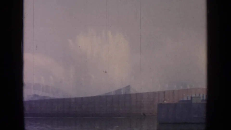 A faded 8mm frame shows Flushing Meadows fountain mist against a curved fairground structure, partially divided by dark window framing.