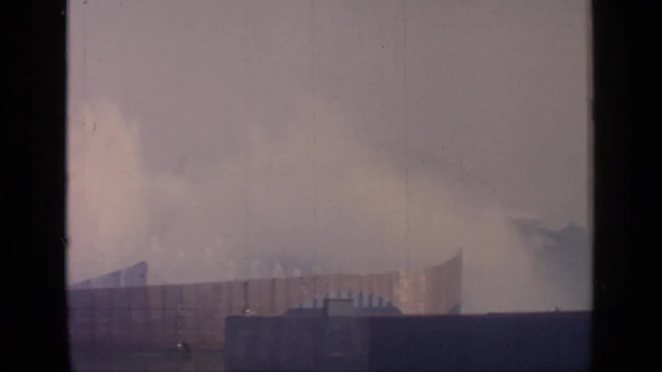 1964 Flushing Meadows view with misty fountain spray, low distant structures, and faded 8mm film texture.