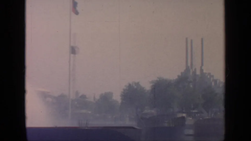 1964 Flushing Meadows landscape with flagpole, fountain haze, trees, and distant vertical stacks.