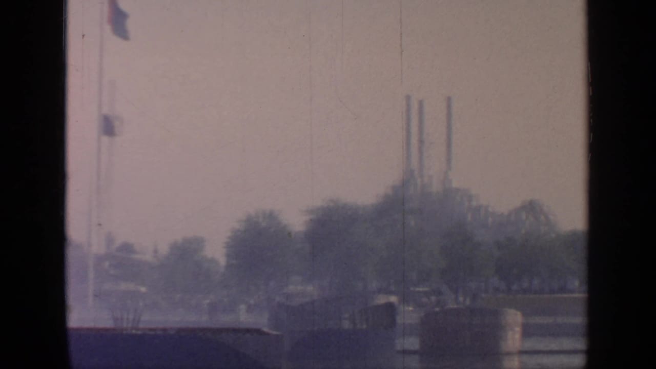 Distant fairground structures across water, partly obscured by trees and haze.