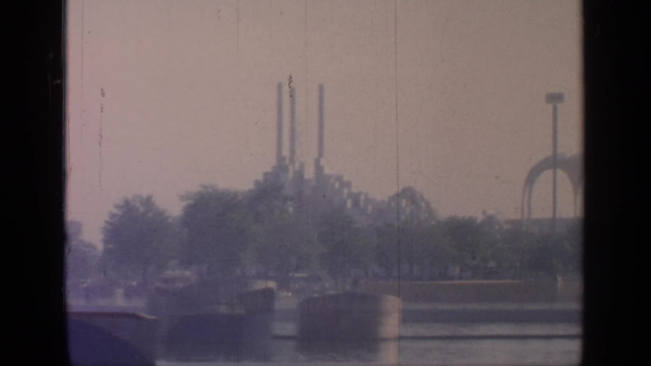 Flushing Meadows waterfront with trees, distant vertical towers, and a tall floodlight-like structure in the background.