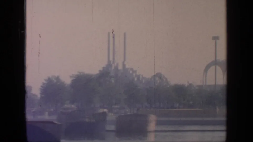 Flushing Meadows waterfront with trees, distant vertical towers, and a tall floodlight-like structure in the background.