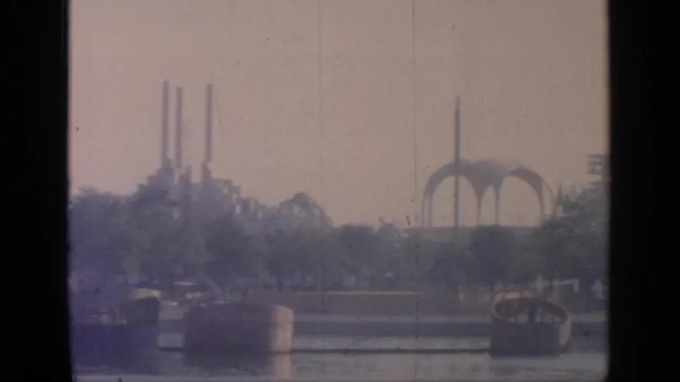 1964 Flushing Meadows park view with water, trees, distant modern arches, and vertical fair structures beyond.