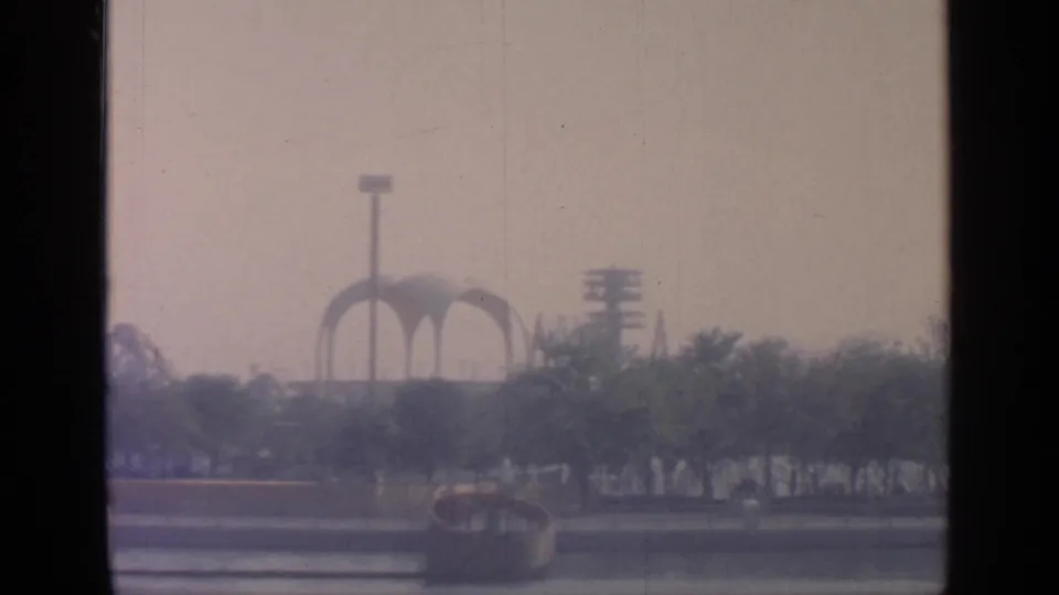 1964 Flushing Meadows fairground view with New York State Pavilion arches behind trees, filmed from a moving vehicle.