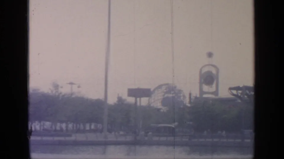 1964 World's Fair grounds at Flushing Meadows, with a tall pole, spherical structure, trees, and distant visitors in a moving 8mm frame.