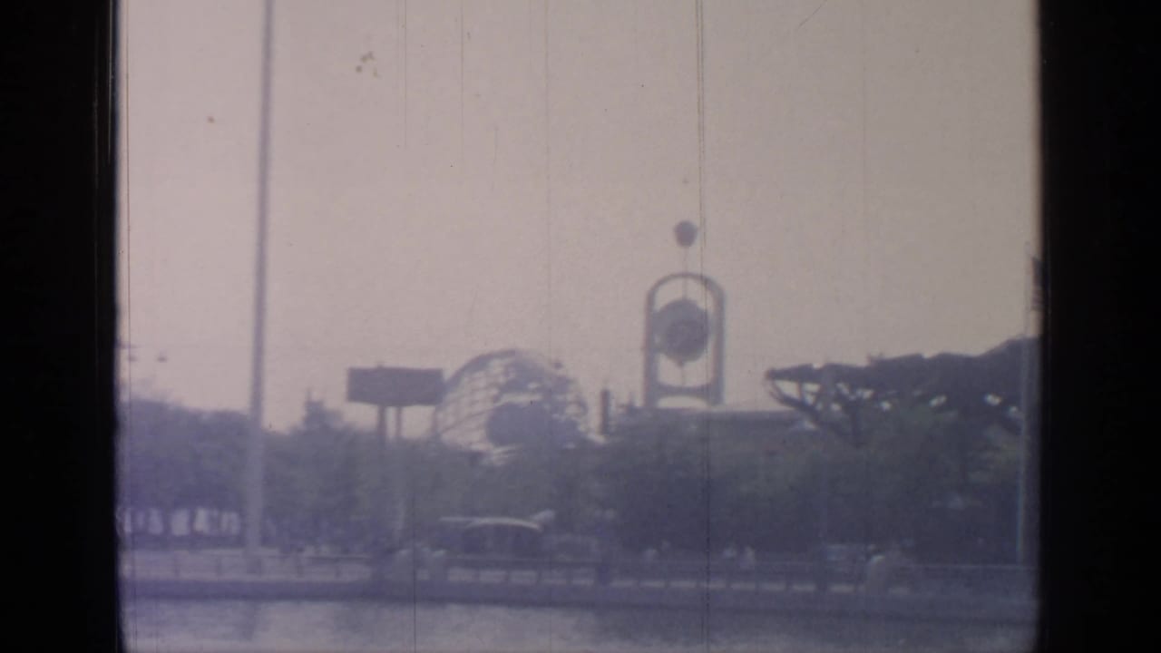 Hazy fairground view through dark window framing with distant structures and trees.