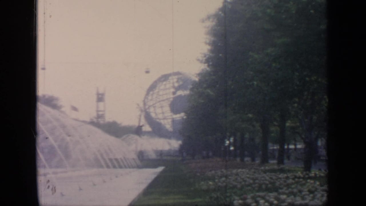 Unisphere and fountains beside trees and a paved fairground walkway.