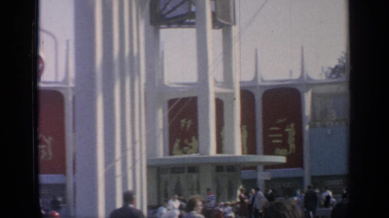 Fairgoers gather near a white pavilion entrance with red panels.