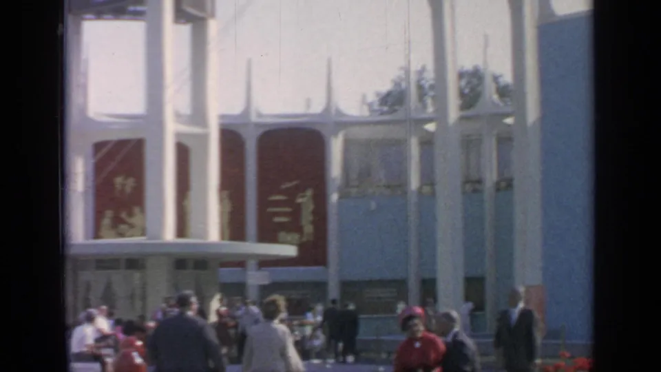 Fair visitors stand and walk before the white Coca-Cola pavilion architecture at Flushing Meadows, with red panels and entrance doors visible.