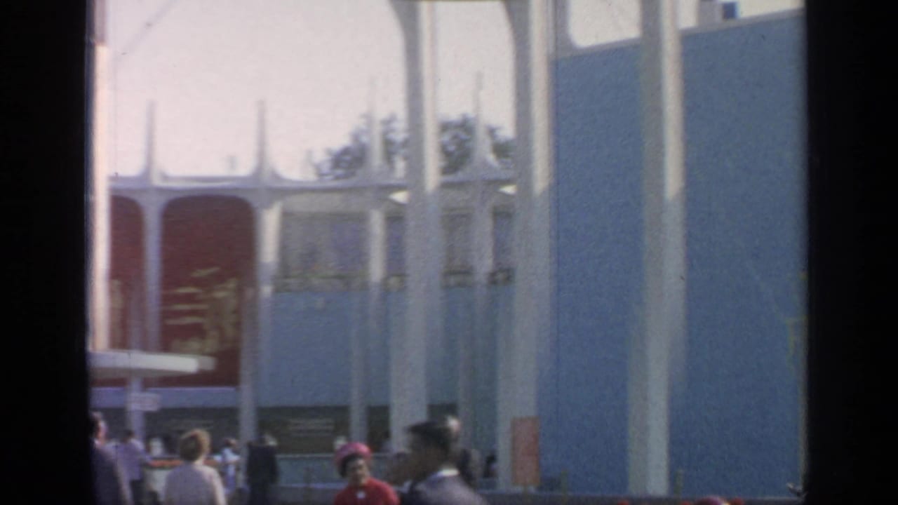 Fairgoers outside a blue and red pavilion with tall white columns.