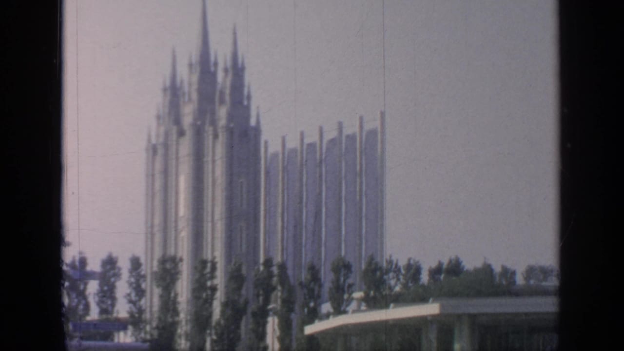 Tall fairground spires rise behind trees under a grey sky.