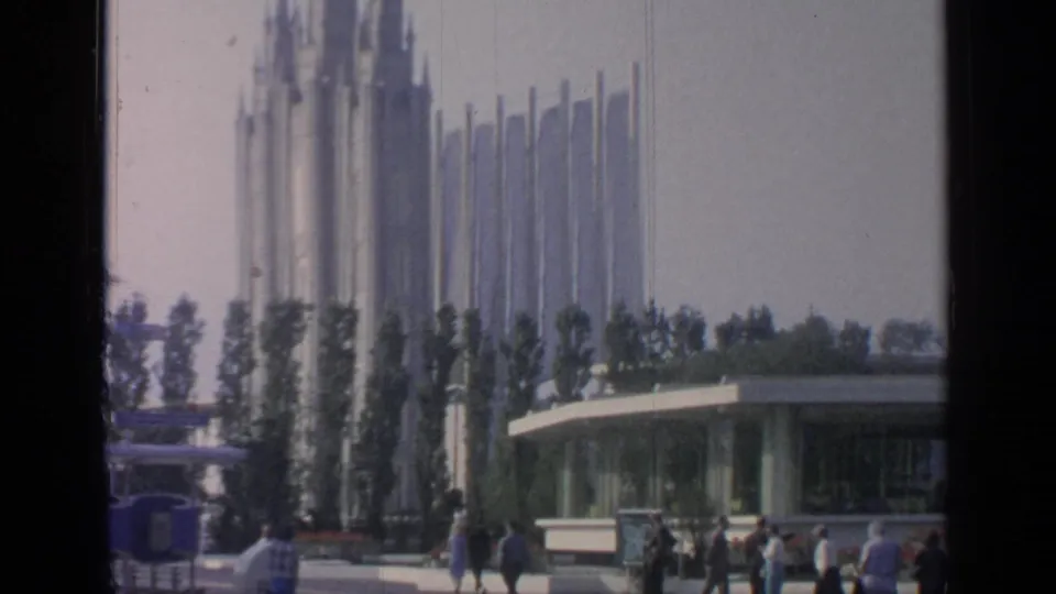 Visitors in 1960s dress move through Flushing Meadows grounds beneath tall pavilion spires and a low glass-fronted structure.
